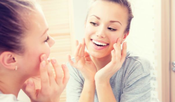 woman smiling while looking in the mirror and touching her face